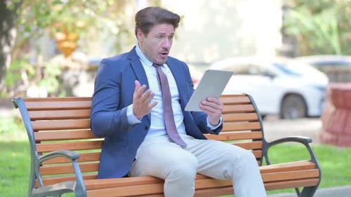 Man Reacts to Tablet While Sitting in Park