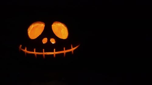 close up sliding shot of a carved orange pumpkin with light candle inside in the dark for the Hallow