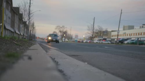 Nearly empty road at dusk in industrial area. Single SUV drives past camera.