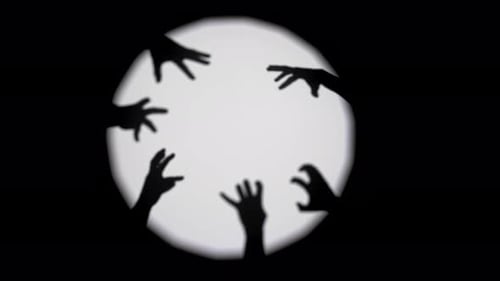 Silhouetted Hands Reaching Against Illuminated Circle