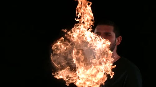 Fire eater breathes inferno rack focus to fiery ball in slow motion studio shot