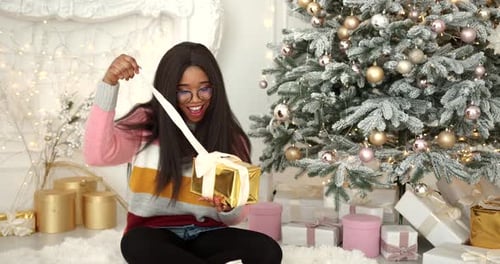 Woman Opening Christmas Present Under Decorated Tree