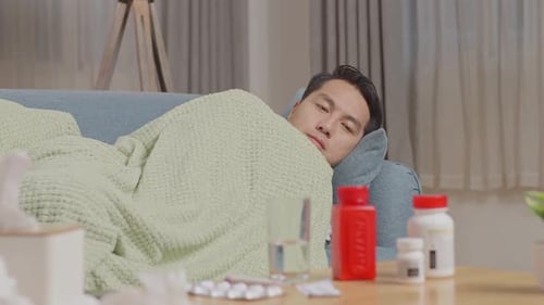 Close Up Of Sick Asian Man With Blanket Freezing And Shiver Lying On Sofa In The Living Room At Home