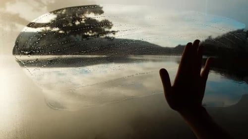Hand Wipes Window Revealing a Mountain Lake at Sunrise