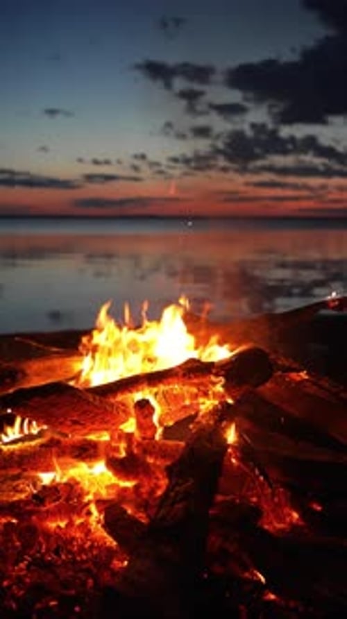 Glowing Bonfire Flames Flickering on Sandy Shoreline Illuminating Serene Lakeside Sunset with