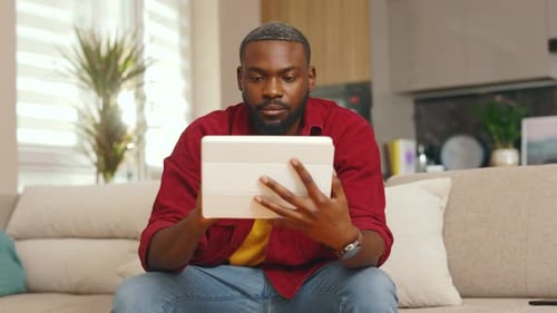 Relaxed African American Young Man Using Digital Tablet Computer at Home Sitting on Sofa Handsome