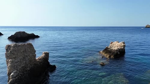Crystal-clear blue sea with rocky outcrops under a clear sky