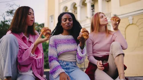 Joyful Moments in the Sun Three Close Friends Savoring Croissants While Relaxing Outdoors in a
