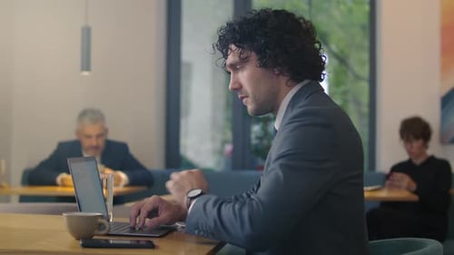Professional Businessman Drinking Coffee and Typing on Laptop in Modern Cafe