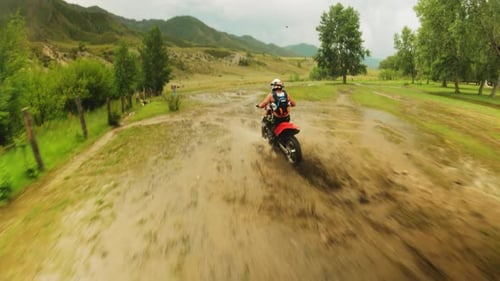 Motorcycle Rider Splashing Through Mud in Rural Landscape