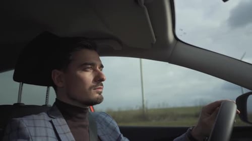man driving a car, shot from interior with wind turbines on background