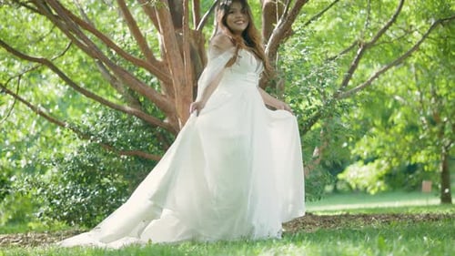 Beautiful Latina Bride with Stunning Wedding Dress Reveal Walking near Green Trees. Summer Outdoor
