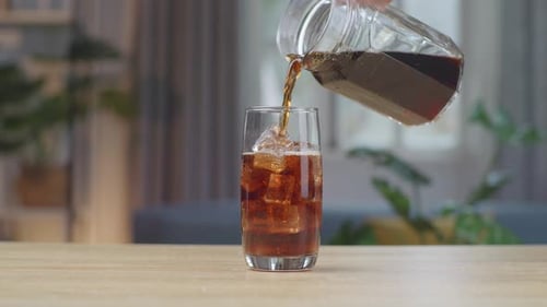 Dark Soda Pouring Into Iced Glass Indoors