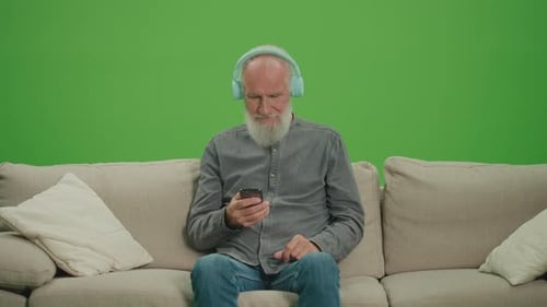 Green Screen An Old Man with a Phone Listens to Music on Headphones