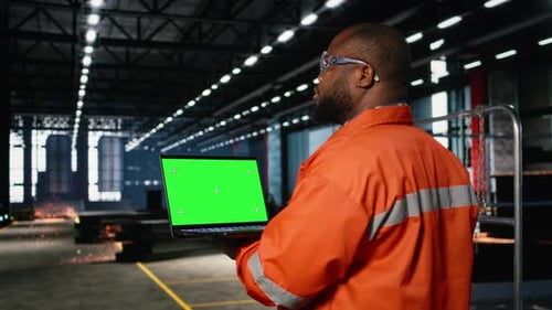 Green Screen Laptop with Black Technician Overseeing Fabrication Tasks