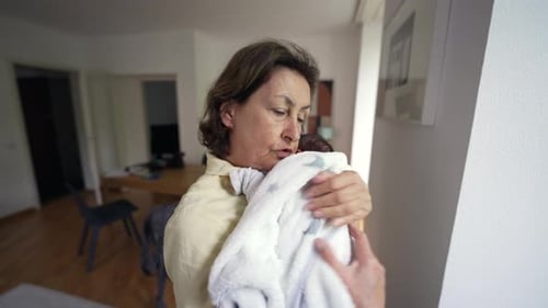 Woman Holding Newborn Infant Wrapped in White Blanket Indoors