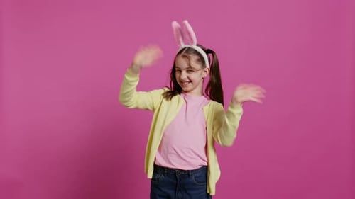 Girl Wearing Bunny Ears Waving on Pink Background