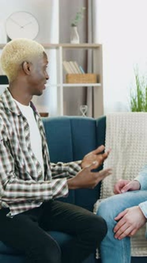 Two Young Men Talking, Hugging on Couch Indoors