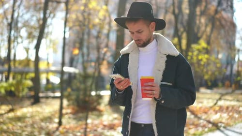Young Absorbed Man Messaging Online in Smartphone App Walking in Sunshine on Autumn Park Alley