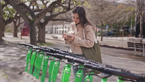 Young Woman Uses Phone Near Electric Scooters