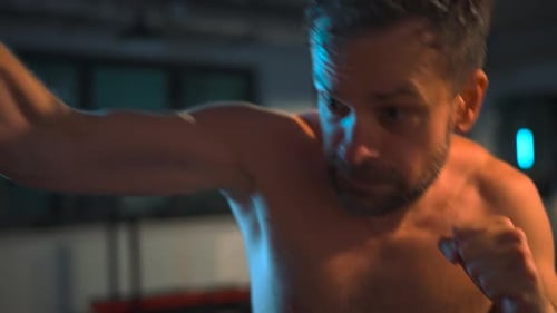 Alone Boxer is Working Out Blows on a Punching Bag in a Gym in Evening