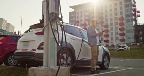 Man Charges an Electric Car at an Electric Charging Station in the City