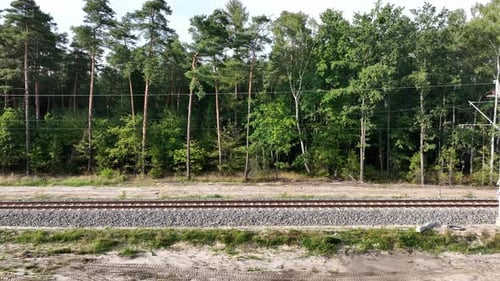 Die Drohnenaufnahme fängt eine Eisenbahnlinie vor einer Waldkulisse ein. Die Kamera bewegt sich parallel zu t
