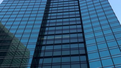 Glass facade of a modern skyscraper reflecting a clear blue sky and neighboring buildings
