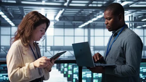 Team of Technicians Working in Server Farm Using Laptops to Analyze Data