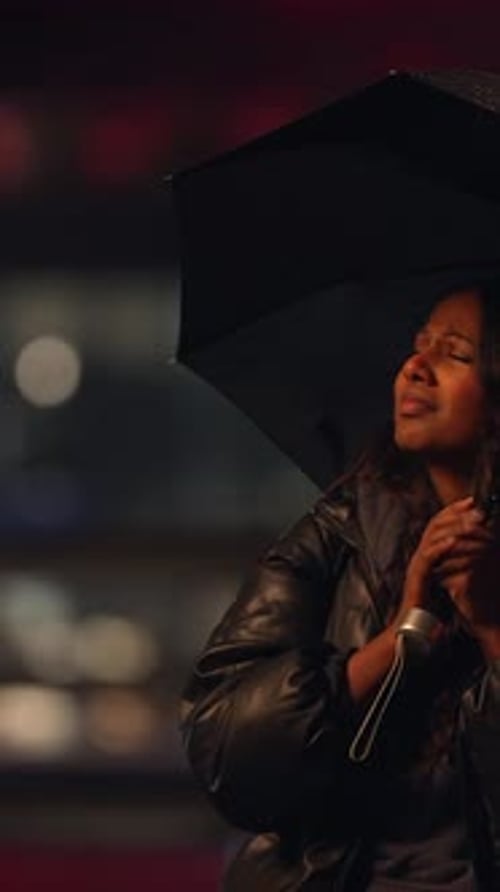 A Woman Stands in the Rain Holding an Umbrella While Using a Microphone for Her Performance