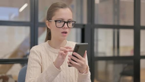 Woman Reacts to Content on Smartphone in Office