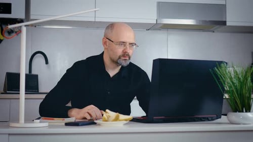 Bearded Adult Man Using Laptop Answering Incoming Mobile Call on Smartphone Studying Online Working