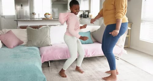 Happy african american mother and daughter having fun dancing in living room, in slow motion