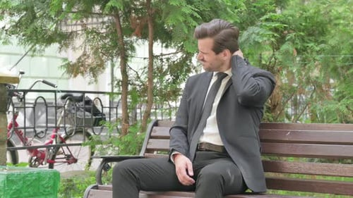 Stressed Man Massaging Neck on Park Bench