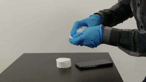 Gloved Hands Clean a Smartphone with Spray