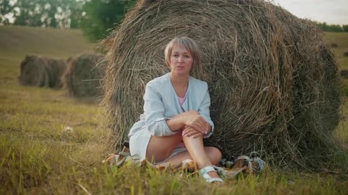 Woman Sits Near Hay Bale in Sunny Field