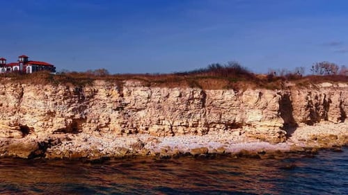 Footage along rocky coast of steep cliffs. View on the beautiful red-roofed house at backdrop.