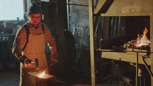 Blacksmith Beating Hot Metal with Sledgehammer on Anvil in Workshop