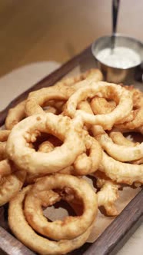 Onion Rings Fried in Flour with Red and White Sauce Laid Out on a Wooden Plate