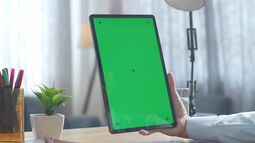 Close up of man's hand using a mock up green screen tablet on a desk