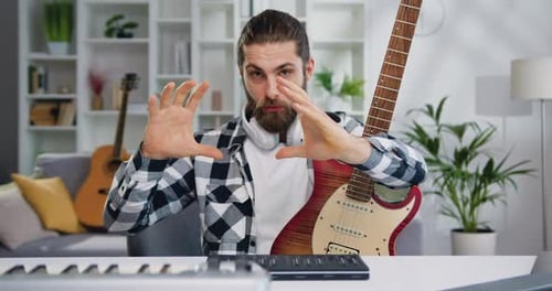 Attractive man talented artist recording video on smartphone sitting of desk in modern studio playin