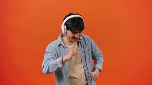 Young Adult Dancing with Headphones Against Orange Background