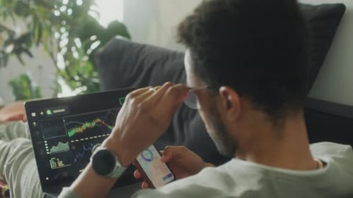 Man Trading Online with Laptop and Phone at Home