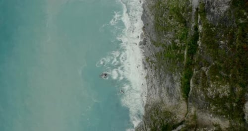Aerial birds eye view overlooking cliff edge rock face & breaking coastal ocean waves splashing agai