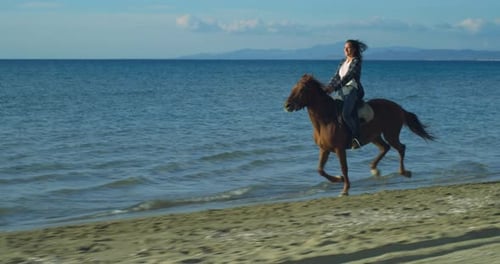 Retrato de uma linda mulher feliz em roupas casuais montando um cavalo galopante à beira-mar