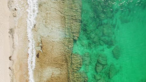 Aerial of sandy beach with turquoise sea water with soft waves and rocky seabed