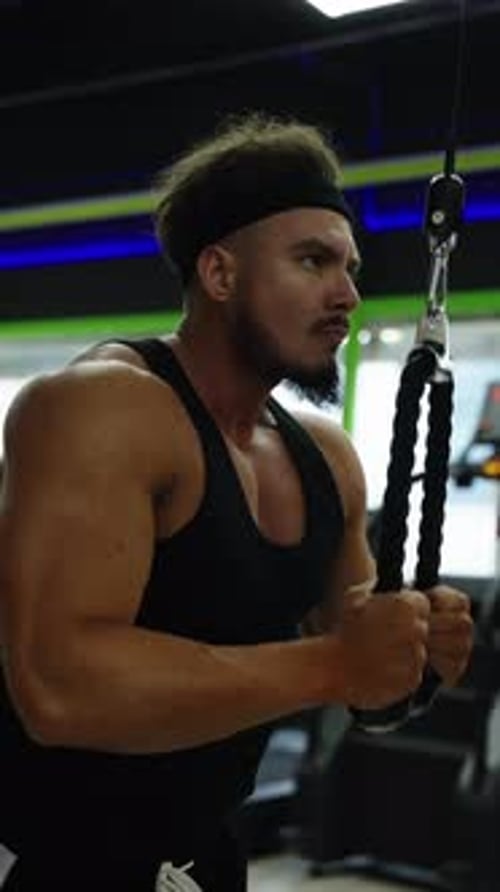 Focused Athlete Performs Cable Triceps Pushdowns in a Modern Gym Showcasing Muscular Arms and