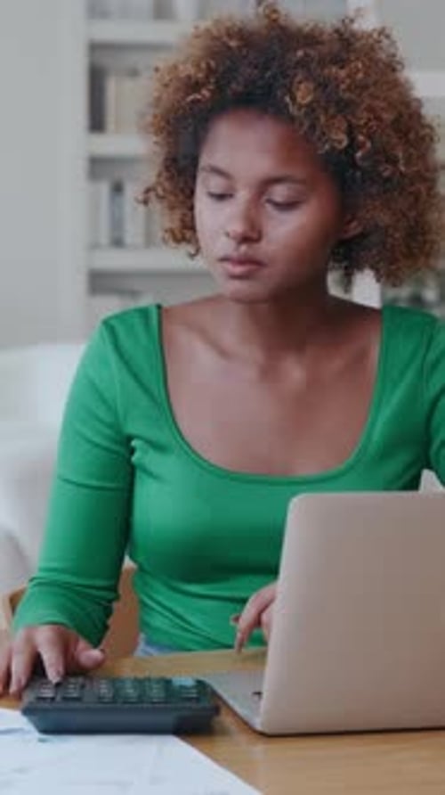 Focused Young Woman Calculates Budgets at Home While Working on a Laptop