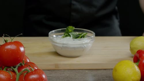 Pieces of Green Leaves Fall Into a White Sauce on the Table Among Colorful Vegetables and Fruits