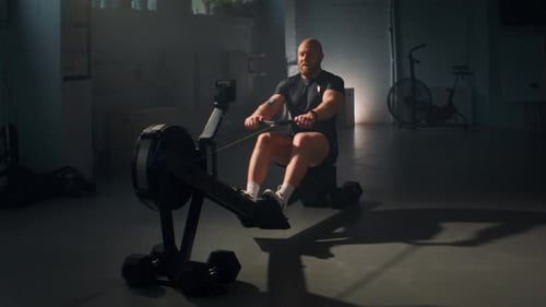 Muscular Man in Sportswear Uses Rowing Machine in Modern Gym